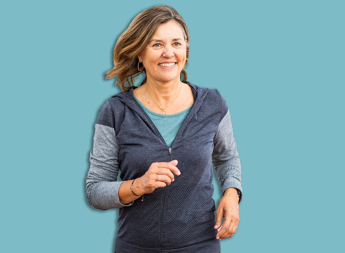 Middle-aged woman runs confidently in sportswear under a covered walkway, enjoying a refreshing outdoor workout with a cheerful expression