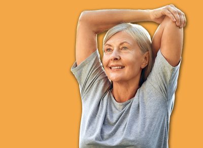 A joyful senior woman is gracefully stretching her arms outdoors in a lush, expansive green park, fully embracing a life of wellness, vitality, and the beauty of nature around her