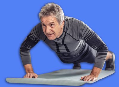 Senior male stays fit by doing pushups on a mat inside the fitness center.