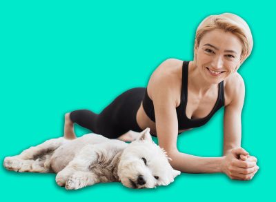 Peaceful blonde lady in black activewear doing yoga practice while tired Westie resting beside on floor of kitchen. Athletic yogini holding Forearm Plank Pose during yoga session with pet at home.