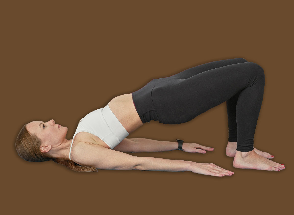 Woman in sportswear on blue mat doing glute bridge with feet planted and hands at sides in studio with exercise balls; calm strength balance.