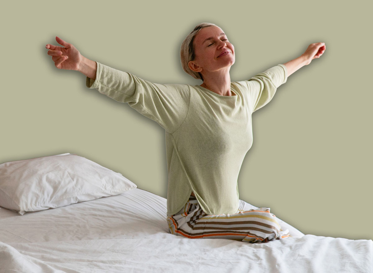 Happy Refreshed Woman 40s waking up from Bed in the Morning by Stretching hands - concept of positive emotion, rejuvenation and relaxation