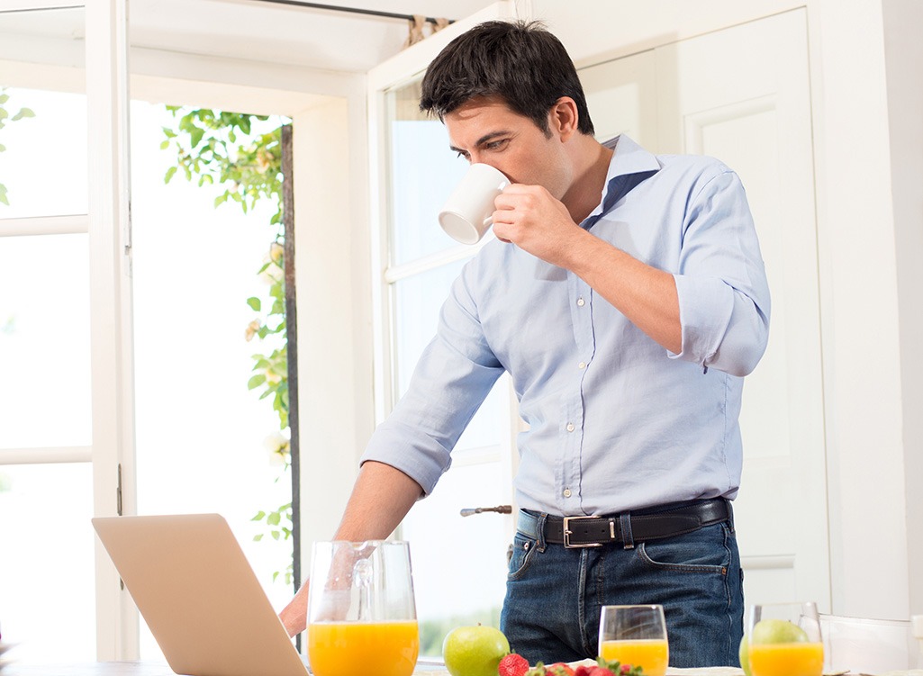 Man drinking coffee and looking at laptop