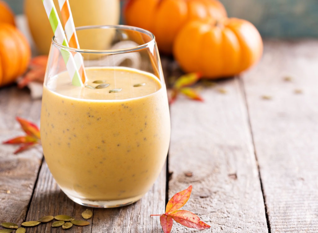 pumpkin smoothie in glass with straw and mini pumpkins