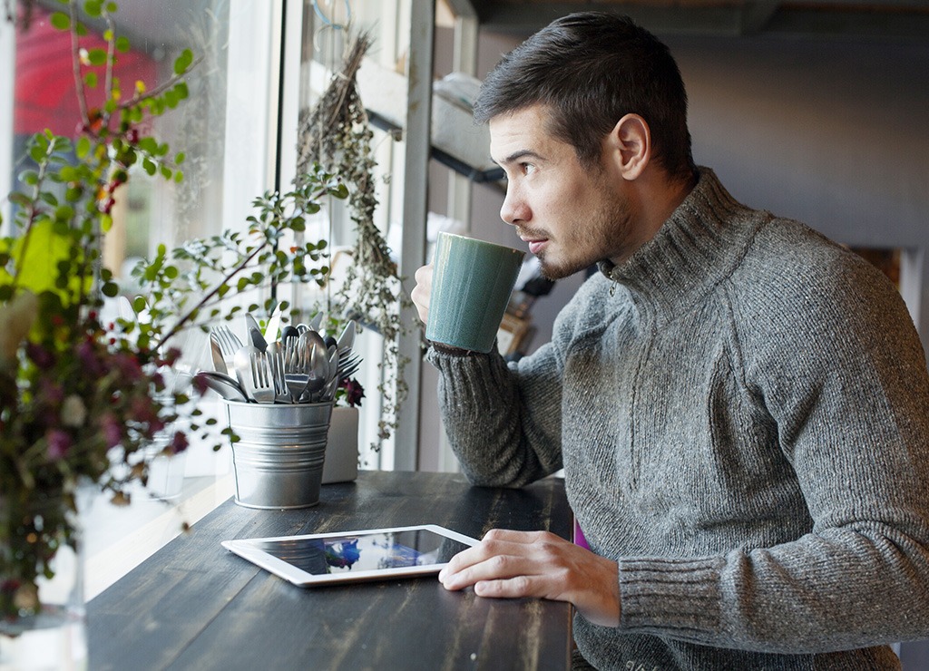 Man reading tablet and drinking coffee at cafe