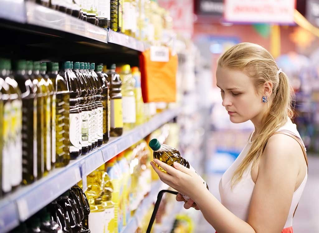 woman shopping at grocery store holding olive oil bottle