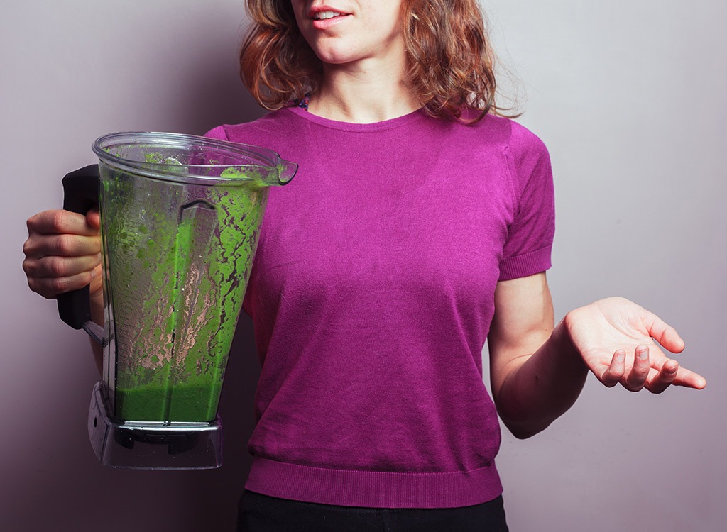 Woman holding blender with green drink