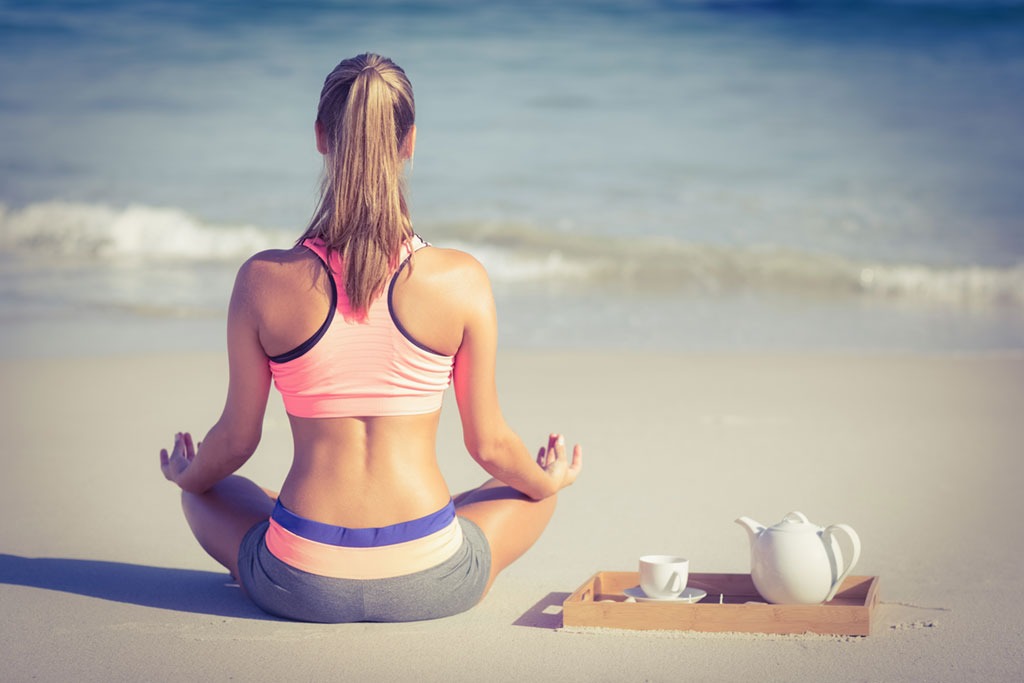 Woman meditating on beach with teapot