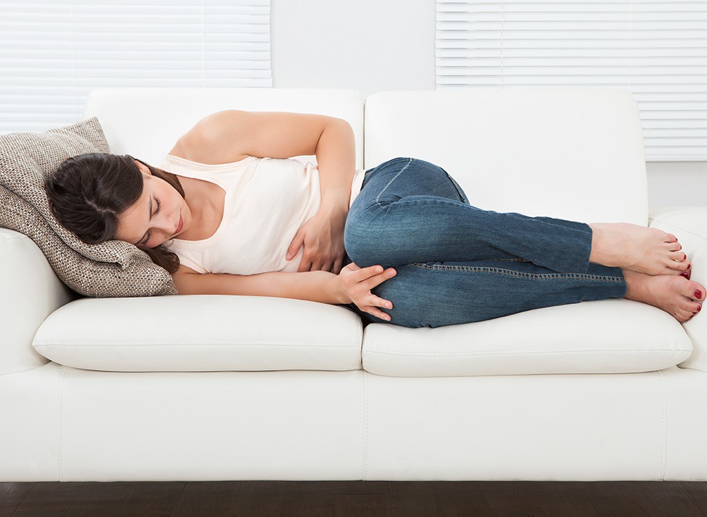 Woman holding stomach on couch