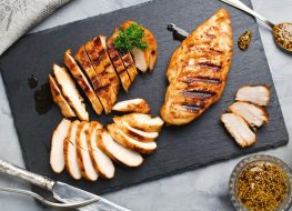 Cut up cooked chicken breast on a dark grey cutting board