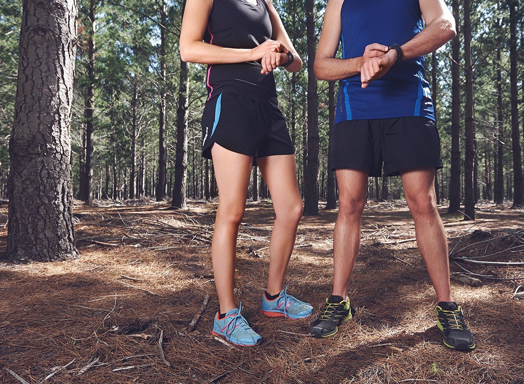 Man and woman checking fitness watches in woods during run