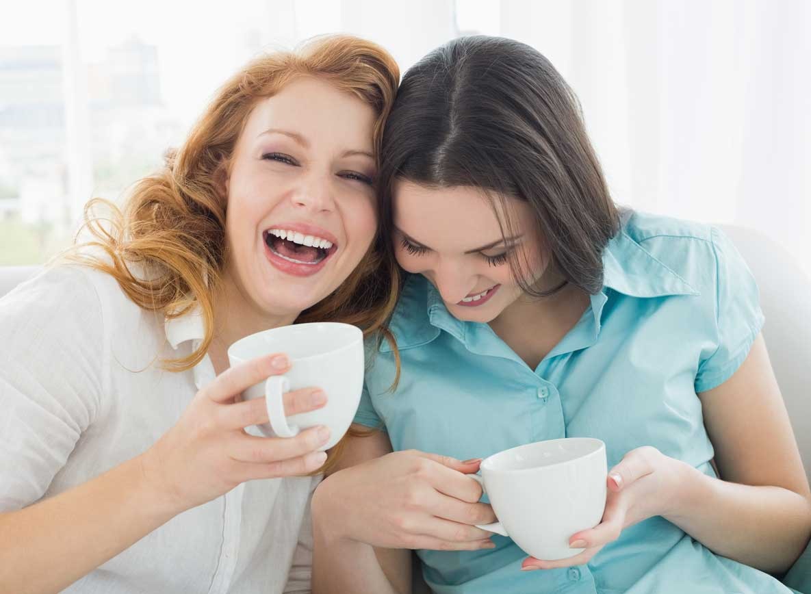 Two women laughing drinking out of mugs